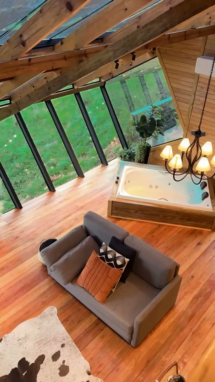 Estar da Cabana Omega sob o telhado de vidro, com sofá e hidromassagem junto à janela