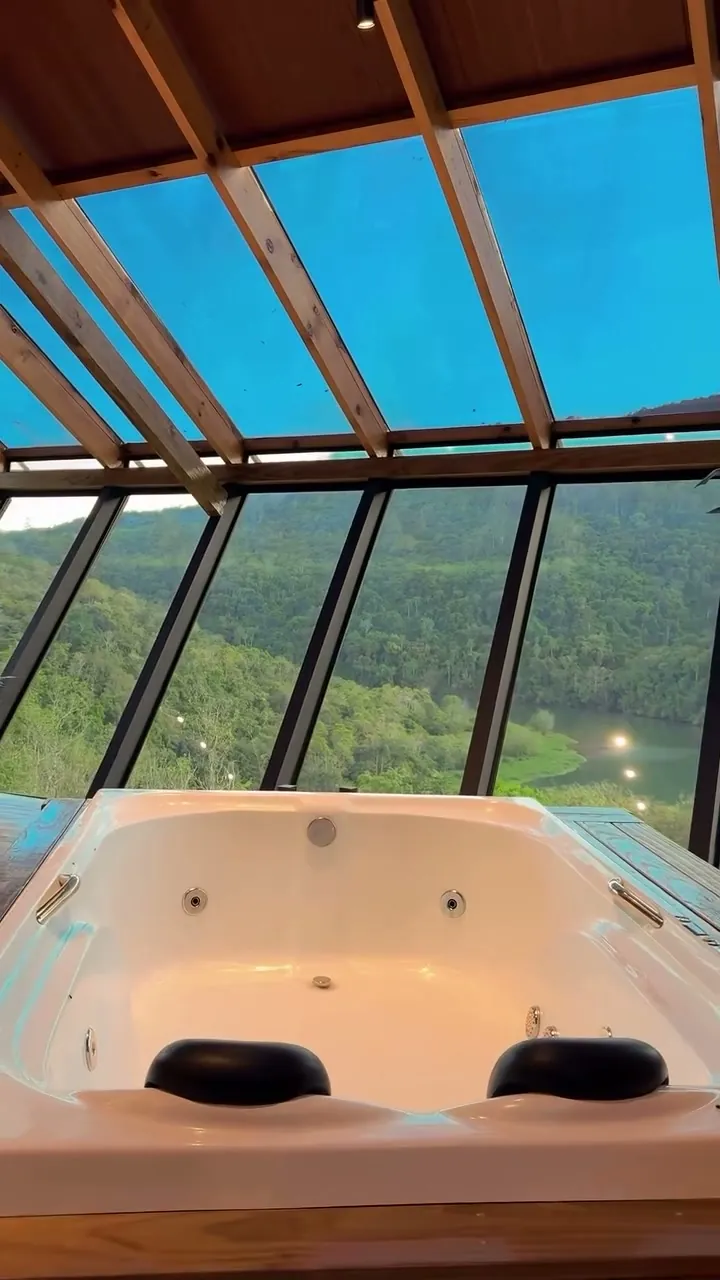 Banheira de hidromassagem da Cabana Omega diante da parede de vidro e da mata
